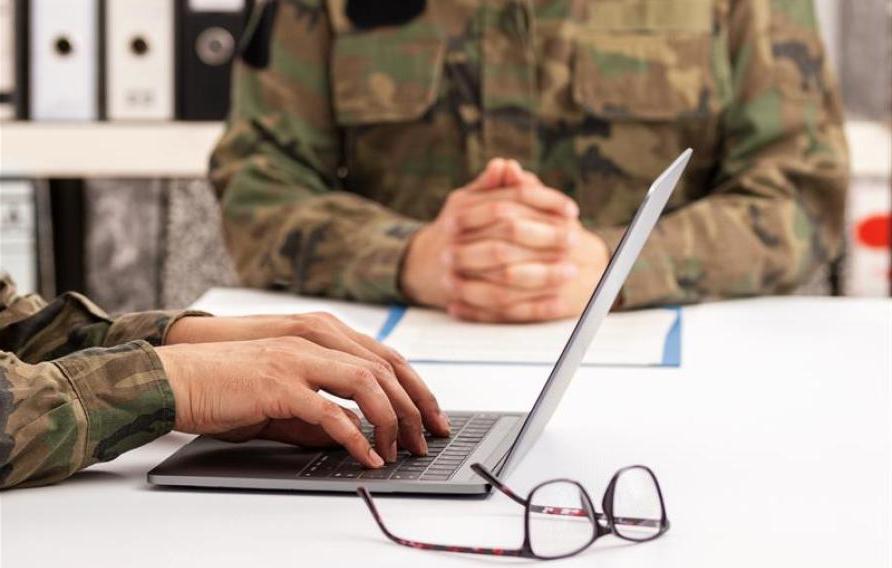 Military officers meet to discuss recruitment. They are using a laptop.